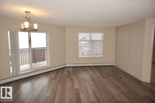 Spacious interior with wood-finish flooring, neutral-toned walls, and a textured ceiling - 326 6076 Schonsee Way, Edmonton, AB - Indoor Photo Showing Other Room