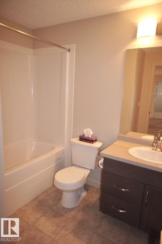 Bathroom featuring a white tub/shower combination, a toilet, a vanity with a light countertop, and tile flooring - 326 6076 Schonsee Way, Edmonton, AB - Indoor Photo Showing Bathroom