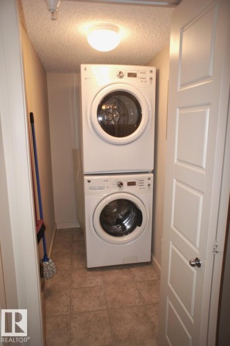 Dedicated laundry area featuring a stacked washer and dryer, tile flooring, and a flush mount ceiling light - 326 6076 Schonsee Way, Edmonton, AB - Indoor Photo Showing Laundry Room