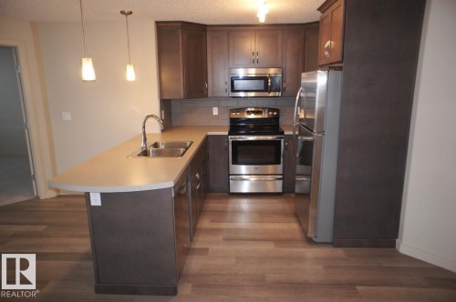 U-shaped kitchen featuring wood-finish flooring and dark wood cabinetry - 326 6076 Schonsee Way, Edmonton, AB - Indoor Photo Showing Kitchen With Double Sink