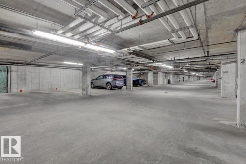 Underground parking garage featuring concrete walls and flooring, exposed ceiling utilities, and overhead fluorescent lighting - 326 6076 Schonsee Way, Edmonton, AB - Indoor Photo Showing Garage