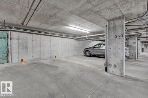 Underground parking space featuring concrete construction, exposed utility piping, and fluorescent lighting - 326 6076 Schonsee Way, Edmonton, AB - Indoor Photo Showing Garage