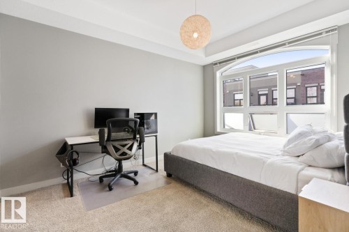 This room offers carpeted floors, a large window with an arched top, and a modern light fixture - 406 10811 72 Avenue, Edmonton, AB - Indoor Photo Showing Bedroom