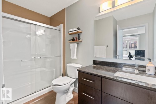 The bathroom features a shower with sliding glass doors, a toilet, and a vanity with a dark countertop and an integrated sink - 406 10811 72 Avenue, Edmonton, AB - Indoor Photo Showing Bathroom
