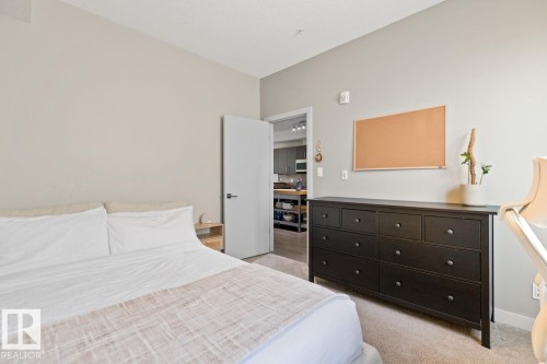 This room features neutral-toned walls, carpeting, and a dark dresser with nine drawers - 406 10811 72 Avenue, Edmonton, AB - Indoor Photo Showing Bedroom