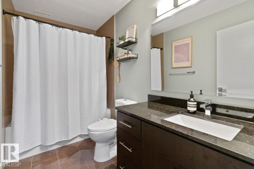 Bathroom featuring a dark wood vanity with a rectangular sink, a dark granite countertop, and a large mirror - 406 10811 72 Avenue, Edmonton, AB - Indoor Photo Showing Bathroom
