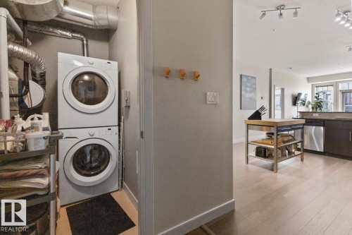 The property features a dedicated laundry area with a stacked washer and dryer, adjacent to an open-concept living space with light-colored flooring and track lighting - 406 10811 72 Avenue, Edmonton, AB - Indoor Photo Showing Laundry Room