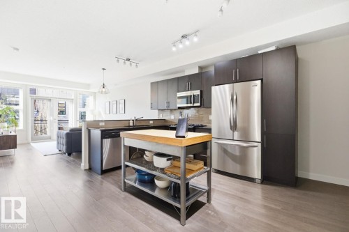 Open-concept living space featuring hardwood floors, stainless steel appliances, and dark wood cabinetry in the kitchen area - 406 10811 72 Avenue, Edmonton, AB - Indoor Photo Showing Kitchen