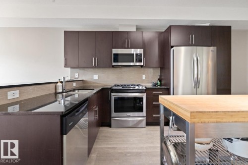 The kitchen features dark wood cabinetry, stainless steel appliances, a black countertop, and a light wood butcher block island - 406 10811 72 Avenue, Edmonton, AB - Indoor Photo Showing Kitchen