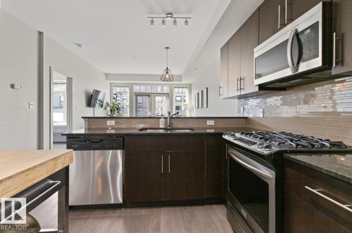 The kitchen features dark cabinetry, granite countertops, a stainless steel dishwasher, and a stainless steel microwave - 406 10811 72 Avenue, Edmonton, AB - Indoor Photo Showing Kitchen