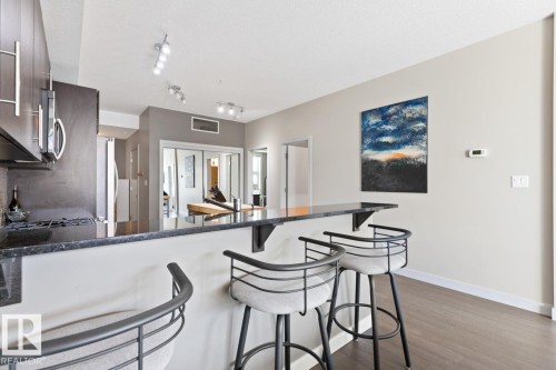 Kitchen featuring a breakfast bar with a stone countertop, dark wood cabinetry, and stainless steel appliances - 406 10811 72 Avenue, Edmonton, AB - Indoor
