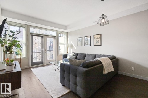 Open concept living space featuring wide plank flooring, a contemporary ceiling light fixture, and a glass-top coffee table - 406 10811 72 Avenue, Edmonton, AB - Indoor Photo Showing Living Room