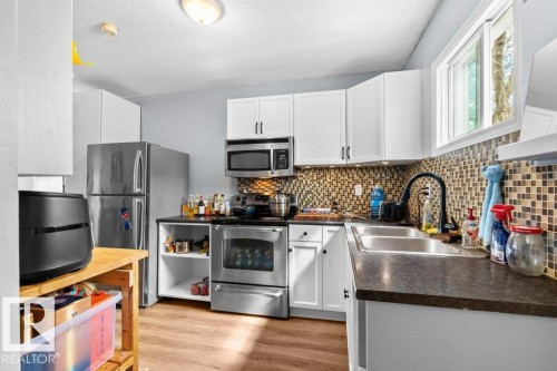 Kitchen with wood-finish flooring, white cabinetry, dark countertops, a mosaic tile backsplash, and stainless steel appliances - 12207 110 Avenue, Edmonton, AB - Indoor Photo Showing Kitchen With Double Sink With Upgraded Kitchen