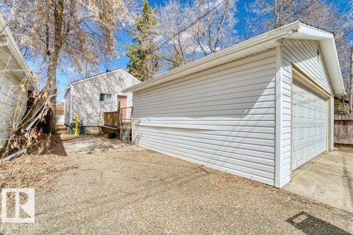 Detached garage featuring white vinyl siding and a paneled overhead door, with a concrete driveway leading to the structure - 12207 110 Avenue, Edmonton, AB - Outdoor