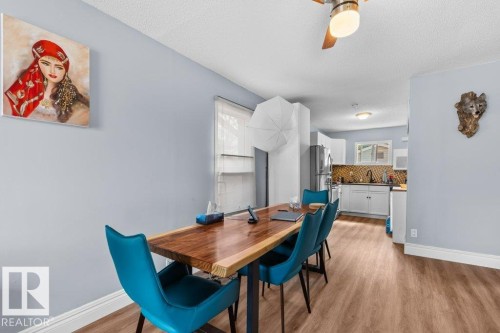 Open-concept dining area featuring wood-finish flooring, a ceiling fan with integrated lighting, and a view into the kitchen with white cabinetry and a patterned backsplash - 12207 110 Avenue, Edmonton, AB - Indoor Photo Showing Dining Room