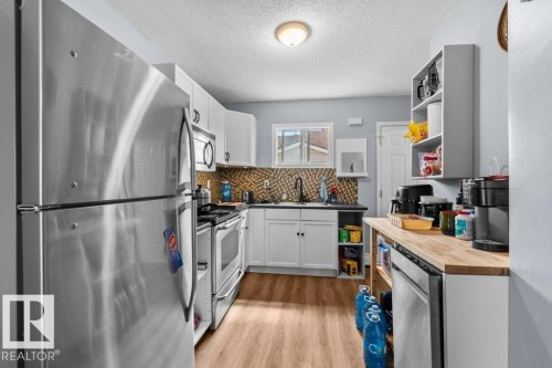 Kitchen featuring stainless steel appliances, white cabinetry, wood-finish flooring, and a patterned backsplash - 12207 110 Avenue, Edmonton, AB - Indoor Photo Showing Kitchen