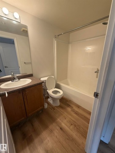 Bathroom featuring wood-finish flooring, a full vanity with an integrated sink and stone-look countertop, and a white tub/shower combination - 104 8119 112 Avenue Nw, Edmonton, AB - Indoor Photo Showing Bathroom