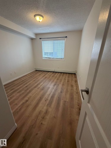 Room featuring wood-finish flooring, a window with horizontal blinds, and a flush mount ceiling light fixture - 104 8119 112 Avenue Nw, Edmonton, AB - Indoor Photo Showing Other Room