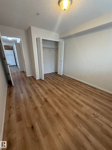 Room featuring wood-finish flooring, a built-in closet with bi-fold doors and wire shelving, and a flush mount ceiling light fixture - 104 8119 112 Avenue Nw, Edmonton, AB - Indoor Photo Showing Other Room