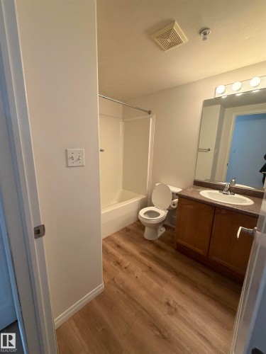 Bathroom featuring wood-finish flooring, a full bathtub with shower, a vanity with integrated sink and dark countertop, and an overhead lighting fixture - 104 8119 112 Avenue Nw, Edmonton, AB - Indoor Photo Showing Bathroom