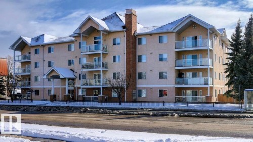 Multi-story residential building featuring a light stucco exterior, multiple balconies with glass railings, a covered main entrance, and pitched roofs - 104 8119 112 Avenue Nw, Edmonton, AB - Outdoor With Facade