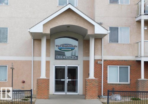 Building entrance featuring a prominent covered portico with white columns, clear glass doors, and a large arched window above - 104 8119 112 Avenue Nw, Edmonton, AB - Outdoor
