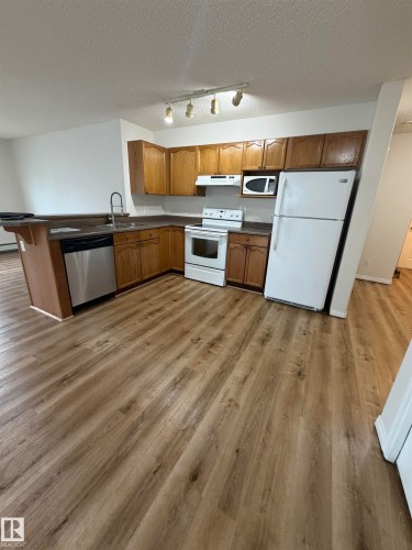 Kitchen area featuring wood-finish flooring, a breakfast bar, wood cabinetry, white appliances, and track lighting - 104 8119 112 Avenue Nw, Edmonton, AB - Indoor Photo Showing Kitchen