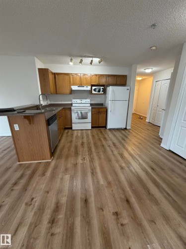 Kitchen featuring wood-finish cabinetry, dark countertops, and a breakfast bar - 104 8119 112 Avenue Nw, Edmonton, AB - Indoor Photo Showing Kitchen With Double Sink