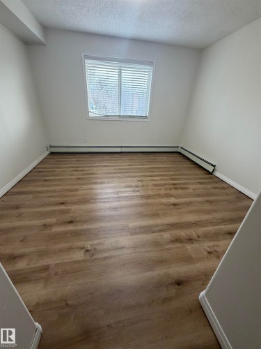 Room featuring wood-finish flooring, a window with horizontal blinds, baseboard heating, white walls, and a textured ceiling - 104 8119 112 Avenue Nw, Edmonton, AB - Indoor Photo Showing Other Room