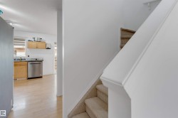 Carpeted staircase with white handrail and partial view of a kitchen featuring a stainless steel dishwasher, wood-finish cabinetry, and light wood-finish flooring - 