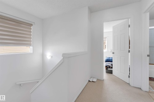 Upper-level landing featuring neutral carpeting, a window with horizontal blinds, and a wall-mounted light fixture - 48 2503 24 Street, Edmonton, AB - Indoor Photo Showing Other Room