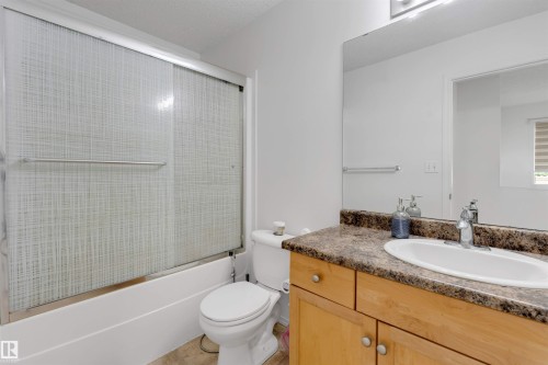 Bathroom featuring a tub and shower combination with sliding textured glass doors, a vanity with wood-finish cabinetry, a white oval sink, and a speckled countertop - 48 2503 24 Street, Edmonton, AB - Indoor Photo Showing Bathroom