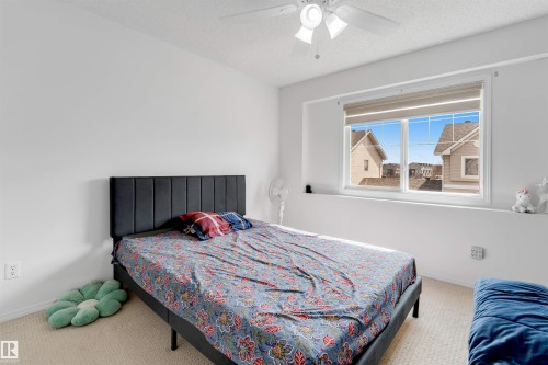 Carpeted bedroom featuring a large window with roller shades, a ceiling fan with integrated lighting, and neutral wall finishes - 48 2503 24 Street, Edmonton, AB - Indoor Photo Showing Bedroom