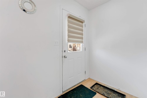 Entry door with lower glass panel and horizontal blinds, set against light-colored walls and wood-finish flooring - 48 2503 24 Street, Edmonton, AB - Indoor Photo Showing Other Room