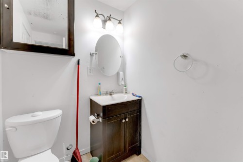 Modern bathroom featuring a white toilet, a dark wood-finish vanity with a white sink, an oval mirror, and a three-light vanity fixture - 48 2503 24 Street, Edmonton, AB - Indoor Photo Showing Bathroom