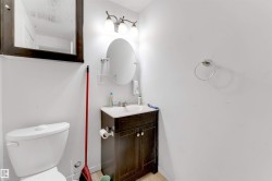 Modern bathroom featuring a white toilet, a dark wood-finish vanity with a white sink, an oval mirror, and a three-light vanity fixture - 