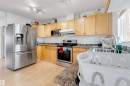 Kitchen featuring wood-finish cabinetry, stainless steel appliances, speckled countertops, and light wood-finish flooring - 48 2503 24 Street, Edmonton, AB  - Indoor Photo Showing Kitchen With Double Sink 