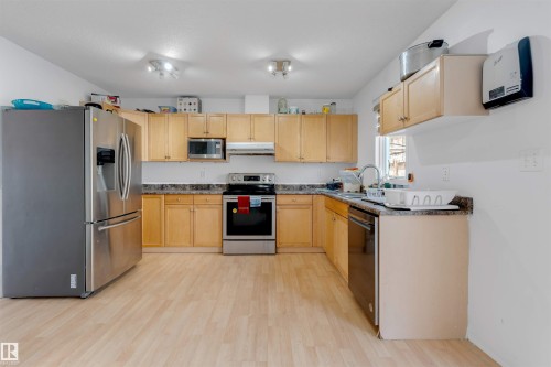 Kitchen featuring extensive light wood cabinetry, stone-finish countertops, and wood-finish flooring - 48 2503 24 Street, Edmonton, AB - Indoor Photo Showing Kitchen