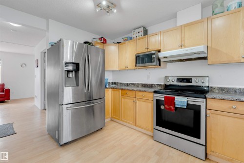 Kitchen featuring stainless steel appliances, wood-finish cabinetry, light-toned countertops, and wood-finish flooring - 48 2503 24 Street, Edmonton, AB - Indoor Photo Showing Kitchen