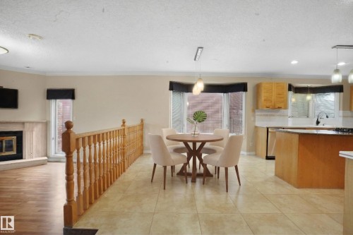 This open-concept living space features light-colored walls, a bay window, and a combination of wood and tile flooring - 10815 Bearspaw Dr E Nw, Edmonton, AB - Indoor Photo Showing Dining Room With Fireplace