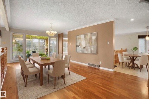 The dining area features hardwood floors, a chandelier, and large windows that provide natural light and views of the exterior foliage - 10815 Bearspaw Dr E Nw, Edmonton, AB - Indoor Photo Showing Dining Room