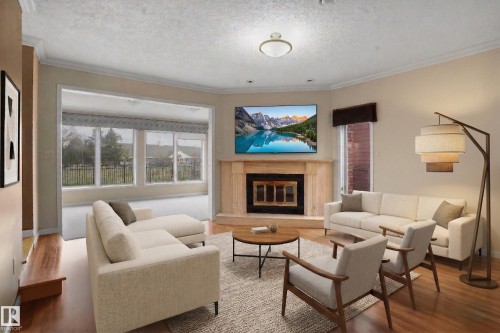 The living room features wood flooring, a fireplace with a light-toned mantle, and crown molding - 10815 Bearspaw Dr E Nw, Edmonton, AB - Indoor Photo Showing Living Room With Fireplace