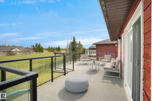 The property features an outdoor patio with a glass railing, providing views of a grassy expanse and distant buildings - 10815 Bearspaw Dr E Nw, Edmonton, AB - Outdoor With Deck Patio Veranda With Exterior