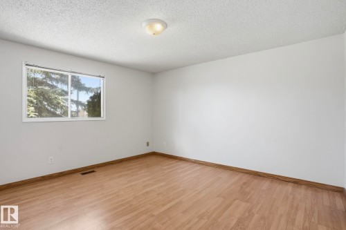 Spacious room featuring wood-finish flooring, white painted walls, a textured ceiling, a flush-mount ceiling light, and a large window - 15811 114 Street, Edmonton, AB - Indoor Photo Showing Other Room
