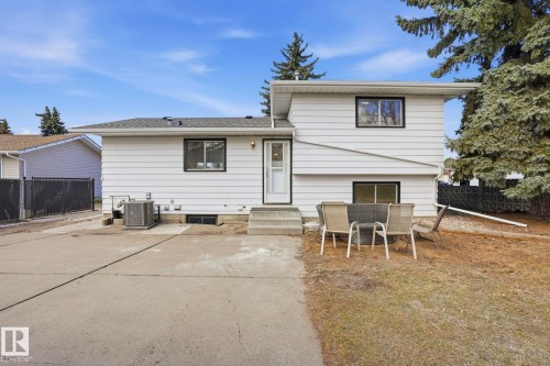 Rear exterior featuring white horizontal siding, black-trimmed windows, a concrete patio area, and mature evergreen trees - 15811 114 Street, Edmonton, AB - Outdoor With Exterior