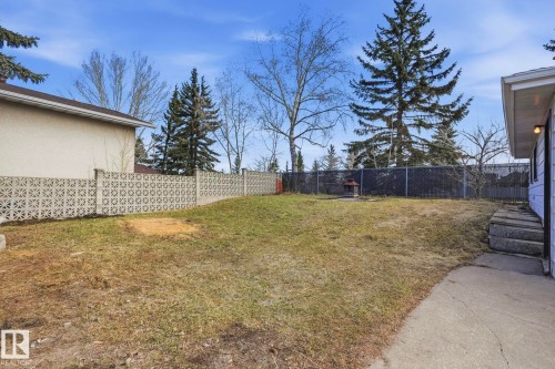 Spacious backyard with mature perimeter trees, a concrete block privacy fence, and a concrete pathway leading to a side entrance - 15811 114 Street, Edmonton, AB - Outdoor