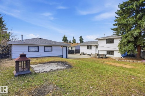 Expansive green space featuring two separate white siding structures with dark trim windows, a gravel patio area, a concrete pad, and mature evergreen trees - 15811 114 Street, Edmonton, AB - Outdoor