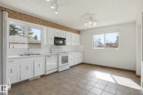 Kitchen featuring white cabinetry with dark hardware, a double basin stainless steel sink, a black built-in microwave, white electric range, and white dishwasher - 15811 114 Street, Edmonton, AB - Indoor Photo Showing Kitchen With Double Sink