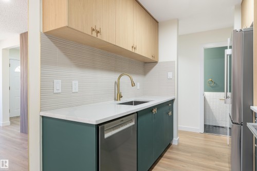 Kitchenette featuring light wood-finish upper cabinetry, teal lower cabinetry with gold-tone hardware, and a white countertop - 15C Callingwood Crest, Edmonton, AB - Indoor Photo Showing Kitchen With Upgraded Kitchen