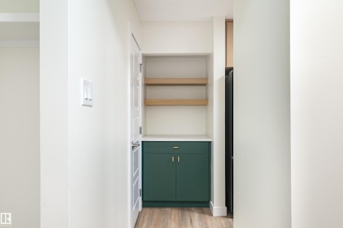 Built-in storage niche featuring dark green cabinetry, a white countertop, two light wood-finish open shelves, and wood-finish flooring - 15C Callingwood Crest, Edmonton, AB - Indoor Photo Showing Other Room